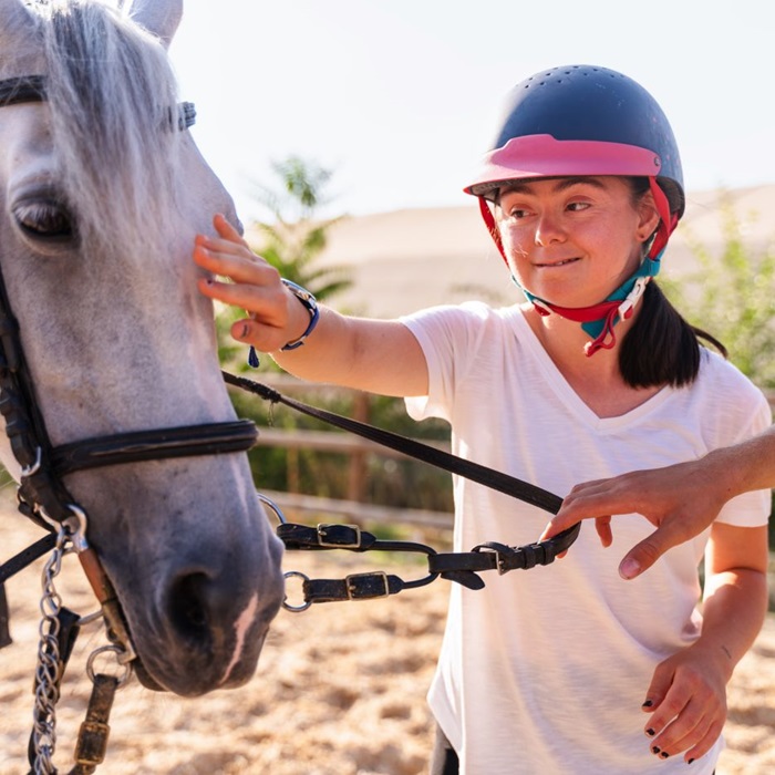 Young girl with Downs Syndrome gently pets a white horse